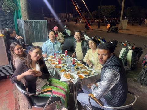       Friends gathered around a table filled with Moroccan dishes at a lively night-time street eatery
  