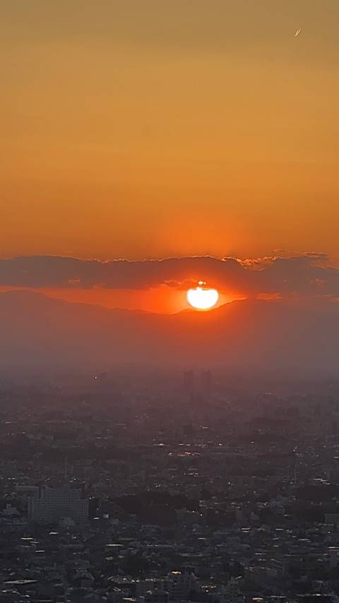      Fiery orange sun setting behind a silhouette of distant mountains with faint cityscape below
  
