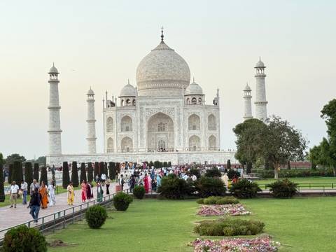       The Taj Mahal at dusk with crowds of visitors walking along the marble pathway.
  