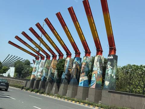      Colorful beam structures adorned with murals lining a roadway in Noida.
  