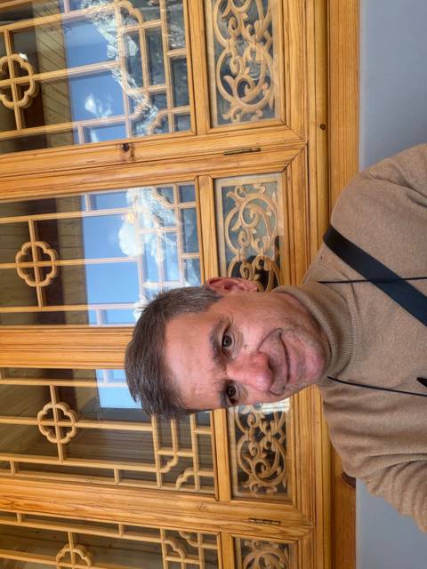       Close-up selfie of a man in a turtleneck with carved wooden window behind him
  