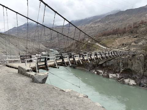       Wooden suspension bridge spans a milky blue river in a rocky mountain valley
  