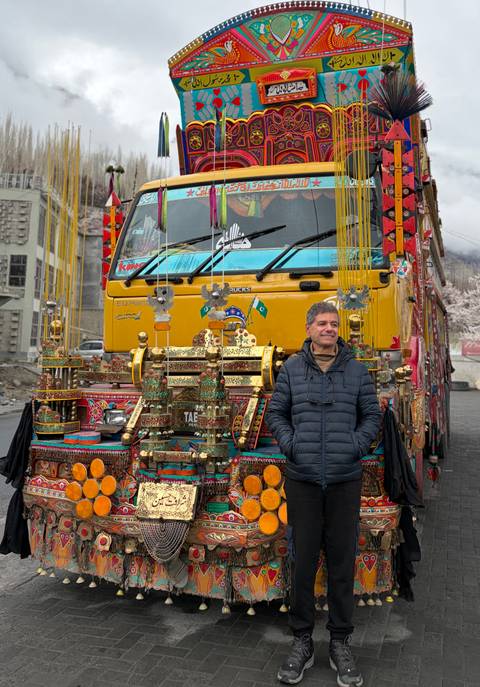       Smiling man stands before brightly decorated Pakistani truck filled with ornaments
  