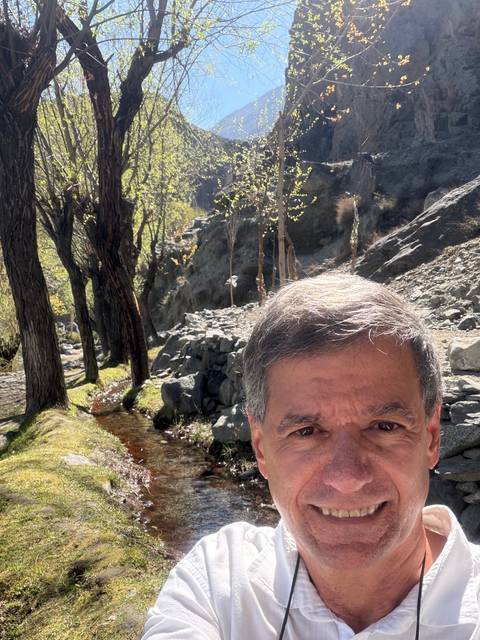       Partial selfie of man with rocky woodland stream and sunlit cliff behind
  