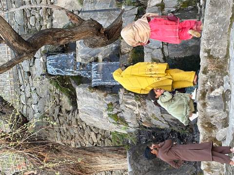       Local children gather near small waterfall on rock ledge, one girl in yellow shawl
  
