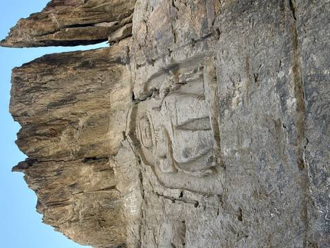       Ancient Buddha bas-relief carved high on rock cliff
  