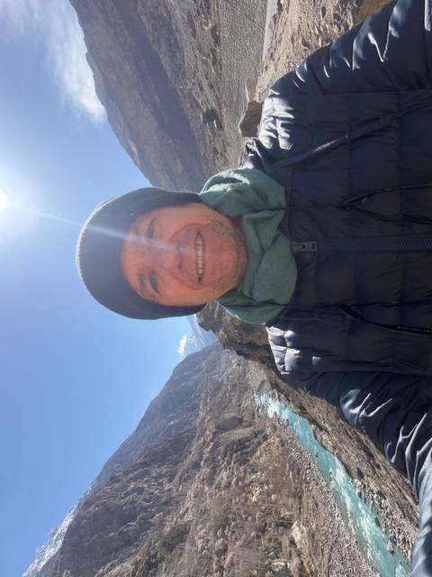       Selfie of man in beanie with sun flare and deep river valley behind
  
