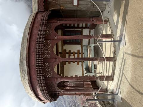       Historic wooden pavilion with ornate carved columns and a stone platform inside a fort courtyard.
  