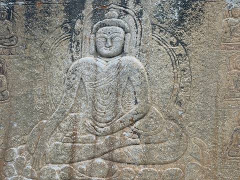       Ancient rock relief of a seated Buddha figure carved into weathered stone.
  