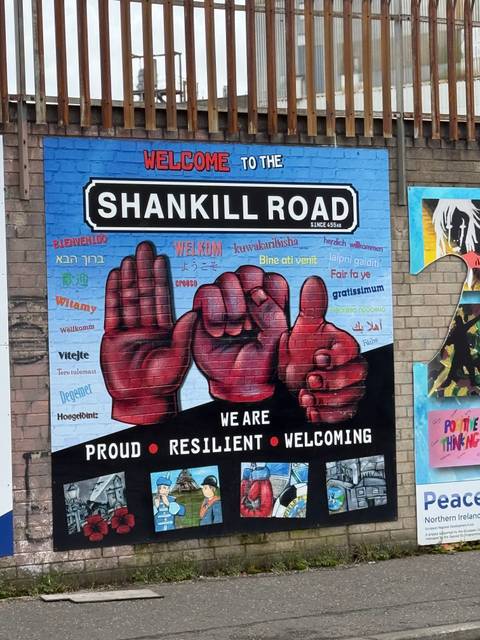       Colourful Shankill Road mural welcoming visitors in multiple languages with painted hands spelling sign language.
  