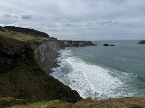       Long stretch of dramatic grey cliffs dropping to crashing Atlantic waves under a brooding sky.
  