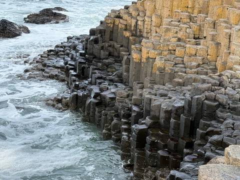       Close-up of the hexagonal basalt columns of the Giant's Causeway with seawater swirling below.
  