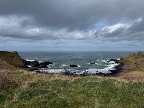       Grassy headlands frame a moody seascape of choppy grey waves under heavy cloud cover.
  