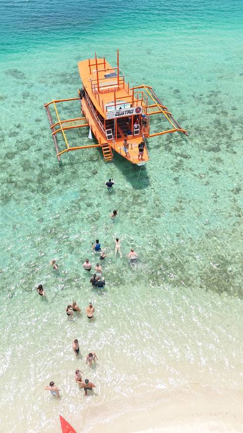       Aerial view of swimmers enjoying crystal-clear shallow lagoon around an orange boat’s ladder.
  