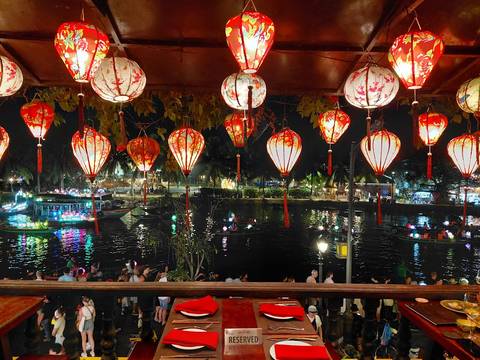       Colorful paper lanterns hanging above a river filled with illuminated boats during a lively night scene.
  