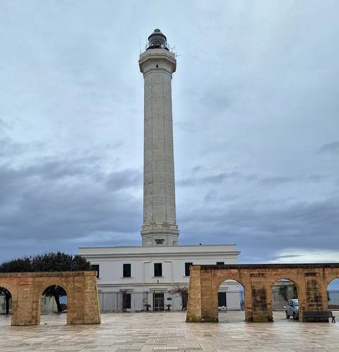       A tall coastal lighthouse and attached building stand beneath a gray sky.
  