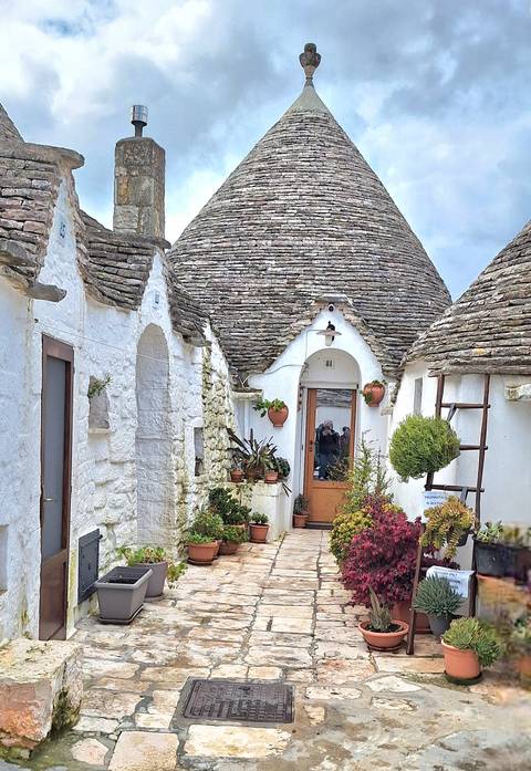       Traditional white-stone trulli houses with conical roofs line a narrow lane.
  