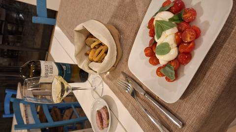       A plate of caprese salad with cherry tomatoes and mozzarella beside wine.
  