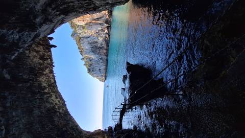       A sea cave frames a vivid view of turquoise water and limestone cliffs.
  