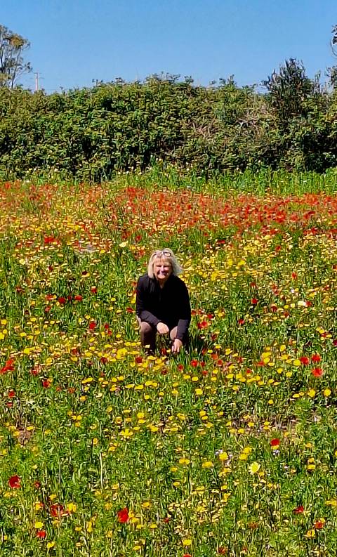       Smiling woman crouches among a vast field of vivid red and yellow wildflowers on a clear day.
  