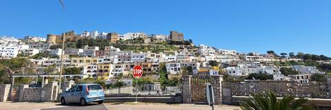       Layered white hill-town with castle ruins rising above colourful houses viewed from a roadside stop sign.
  