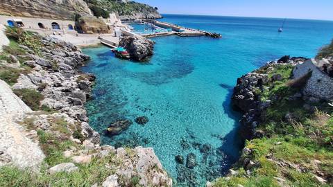       Rocky cove with crystal-clear azure water and a small harbour nestled between cliffs.
  
