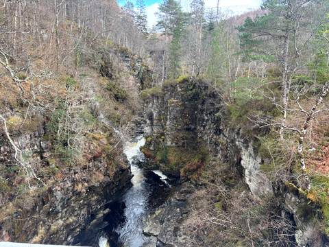       Deep wooded gorge with a fast-flowing river cutting through mossy rock walls in the Highlands
  
