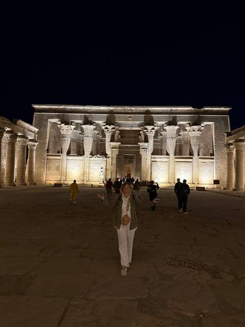       Night view of Kom Ombo Temple illuminated with tourists walking in the grand forecourt.
  