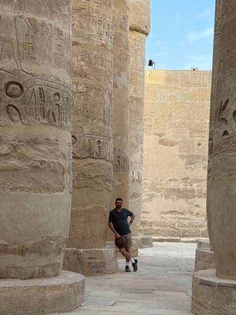       Man posing among giant hieroglyph-covered sandstone columns inside Karnak Temple
  