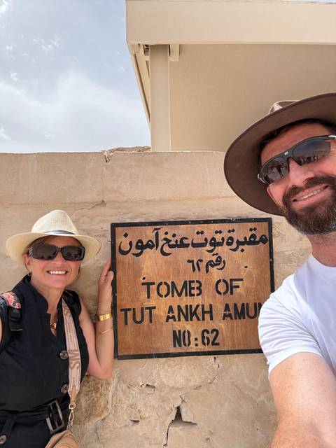       Couple smiling next to the wooden sign for the Tomb of Tutankhamun
  