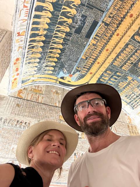       Selfie of travelers beneath colorful hieroglyphic ceiling artwork inside an Egyptian tomb
  