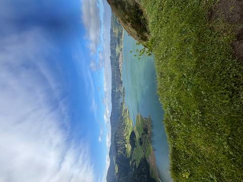       Vivid green crater lake set beneath rolling farmland and dramatic clouds seen from grassy rim
  