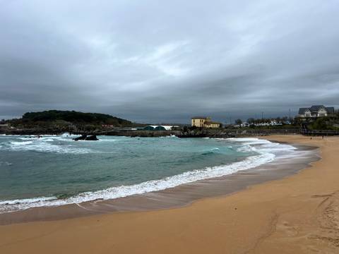       Small cove with turquoise waves crashing onto golden sand beneath a grey sky.
  