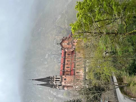       Historic pink stone basilica with twin spires rising against misty mountain backdrop and forested slopes.
  