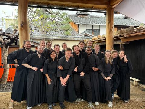       Tour group dressed in black samurai robes smiling together in a traditional wooden courtyard.
  