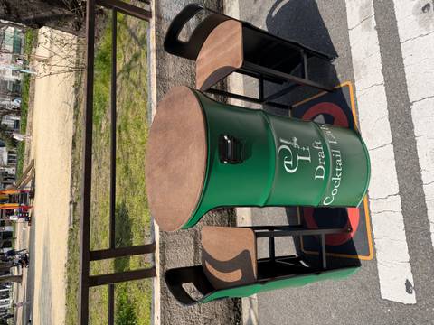       Green metal barrel repurposed as a cafe cocktail table between two high stools on a city street.
  