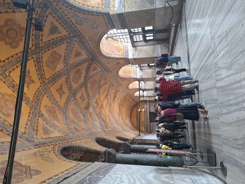       Visitors gather beneath ornate arched ceilings richly decorated with golden mosaics inside a historic building.
  