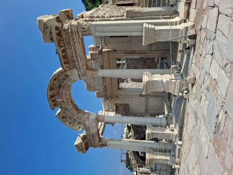       The ornate marble arch and columns of the Temple of Hadrian stand beneath a bright blue sky.
  