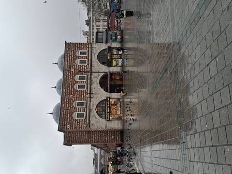       A historic brick bazaar building reflected on a wet plaza during a rainy day.
  