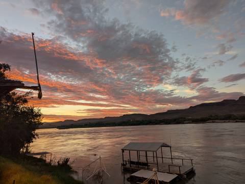       Colorful evening clouds reflect on a wide calm river flanked by low hills at sunset.
  