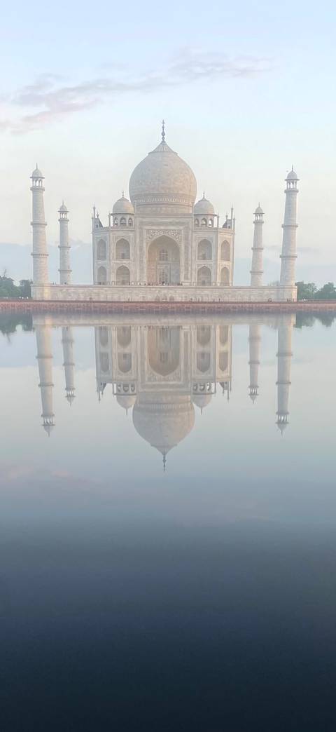       A perfectly still reflection of the Taj Mahal appears upside-down in calm water on a misty morning.
  