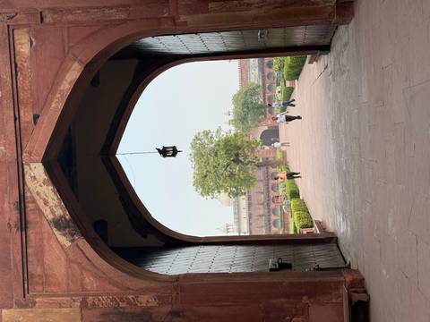       Visitors walk through an arched sandstone gateway onto spacious Mughal gardens.
  