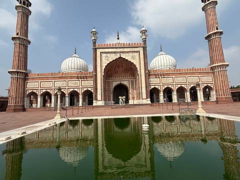       The grand façade and minarets of Jama Masjid reflected in a green courtyard pool.
  