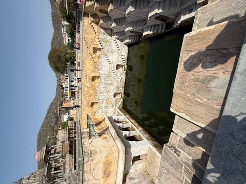       A historic stepwell with tiered arches surrounds a deep green water tank.
  