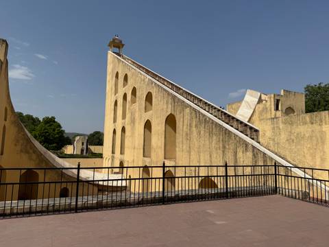      The towering yellow walls and precise angles of Jantar Mantar astronomical instruments under a clear sky.
  