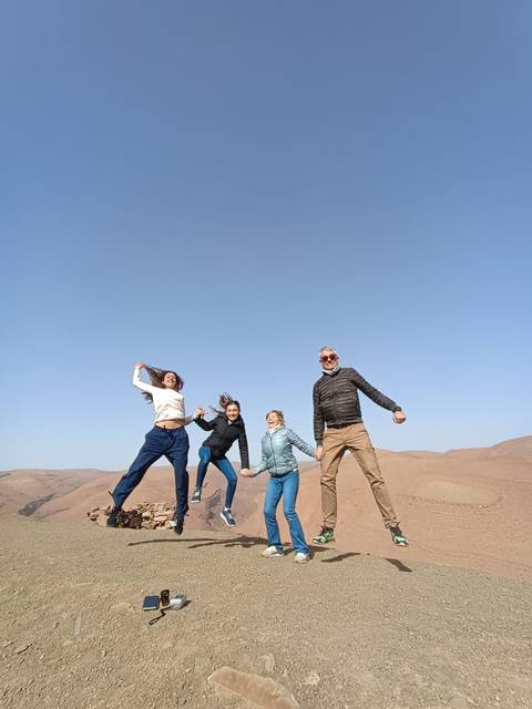       Four friends jump joyfully atop rolling desert hills under a clear blue sky.
  