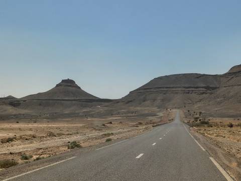       A lonely asphalt road stretches through a barren desert landscape towards distinctive mesas.
  