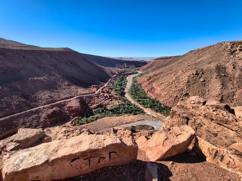       A winding green river oasis snakes through steep red rock canyons beneath a vivid blue sky.
  
