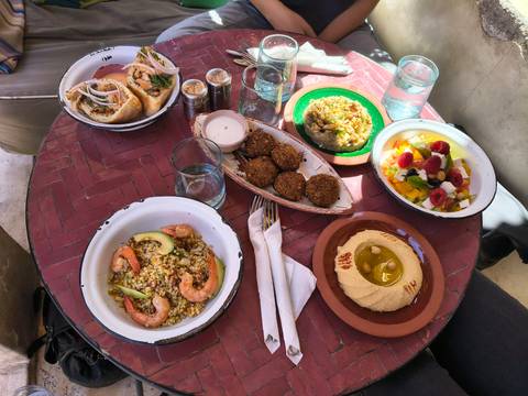       A colorful Moroccan meal spread on a small round table in dappled sunlight.
  