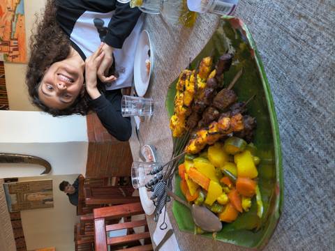       A smiling diner poses behind a plate of skewered meat and vegetables in a casual restaurant.
  